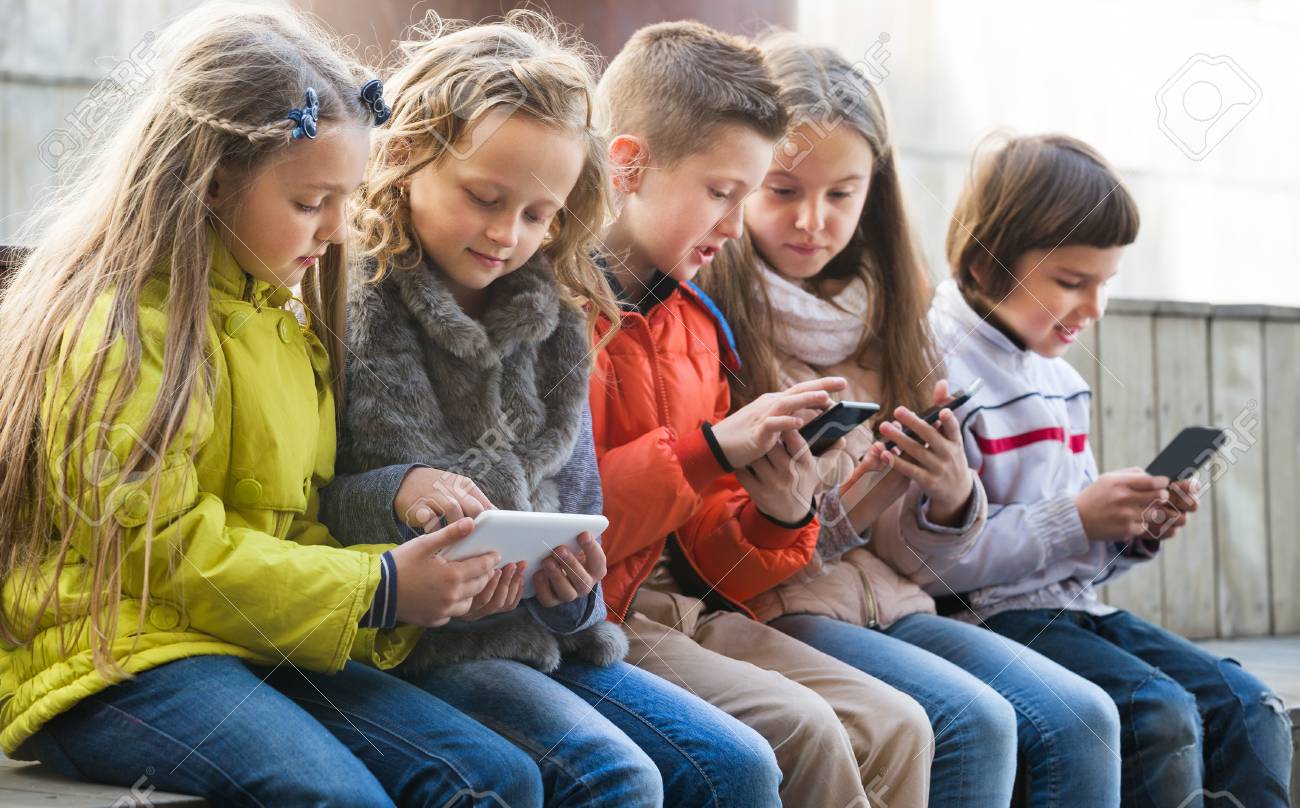 Happy kids sitting on bench with mobile devices